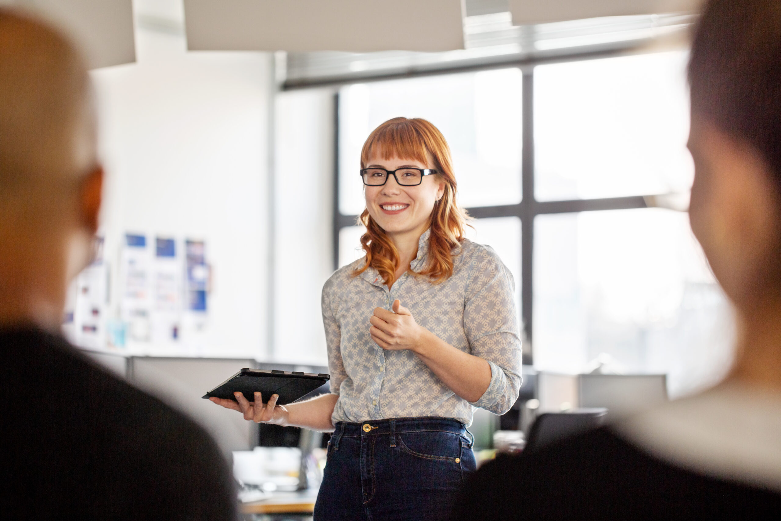 Young businesswoman sharing her views with team in office meeting. Woman professional with digital tablet talking with coworkers sitting in front.